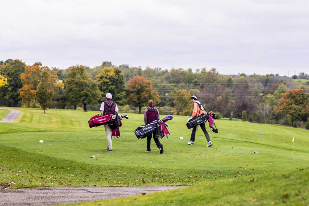 three golfers walk with their bags on a golf course