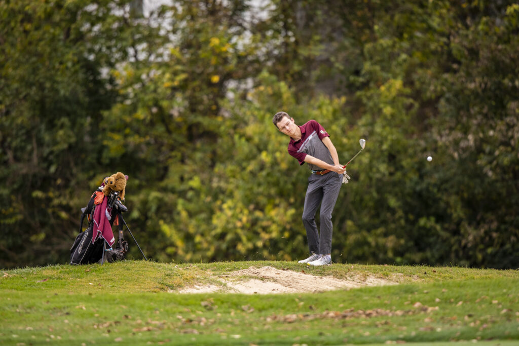 an EKU golfer hits a ball past a sand trap