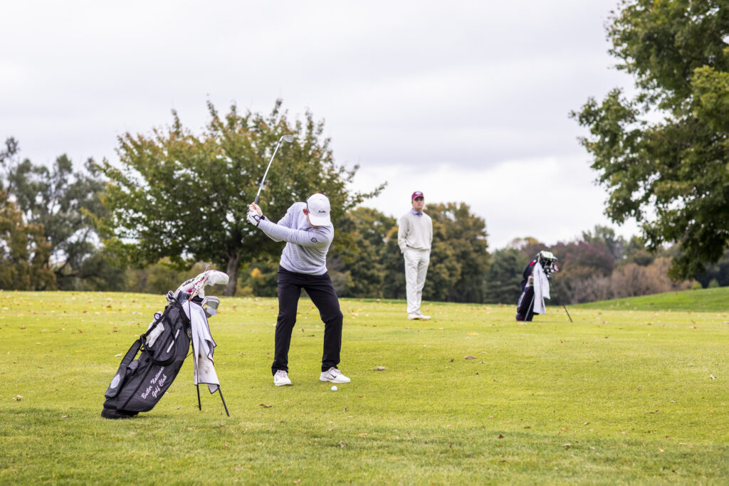 a golfer prepares to hit a ball on a golf course while another golfer looks on