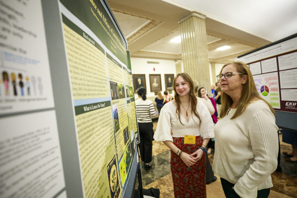 a faculty member looks at a student's display on Scholars Day