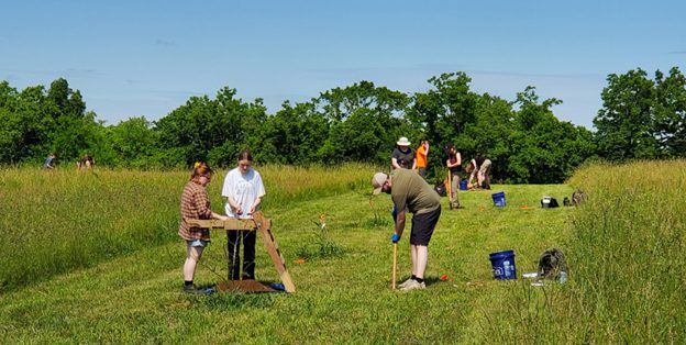 Students and teacher conducting a dig in a field
