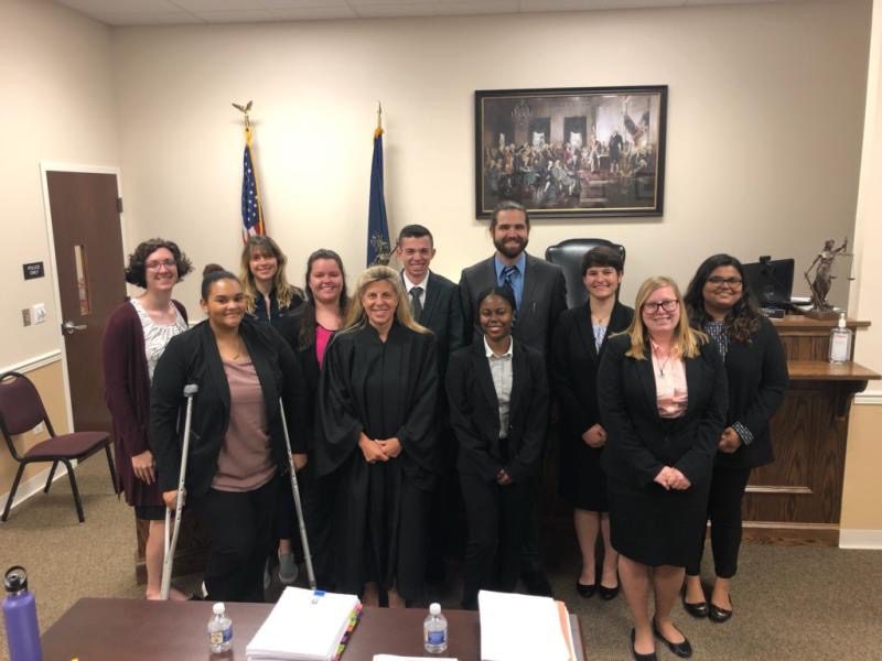 Student interns and court officials pose for a photo in a courtroom.