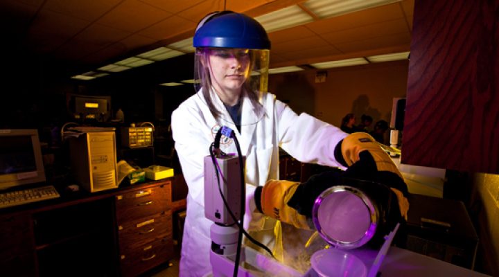 A student wearing protective face gear utilizes forensic equipment.