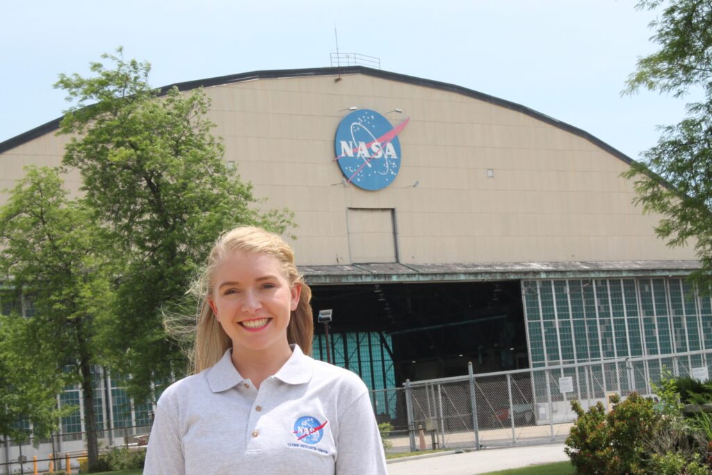 An image of a girl wearing a white NASA polo standing in front of NASA.
