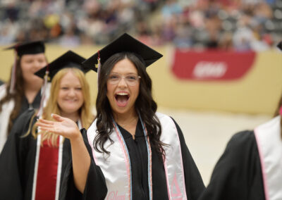 a student shows a big smile and waves during the commencement ceremony procession