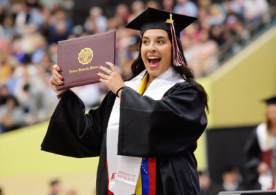 a student holds up their diploma cover with a big smile