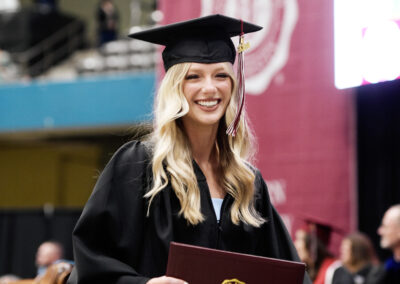 a student smiles as she holds her diploma cover