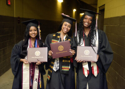 three students pose with their diploma covers after commencement