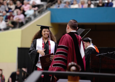 a student walks toward President McFaddin with their diploma