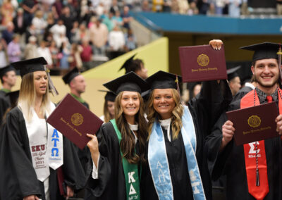 smiling students hold up their diploma covers