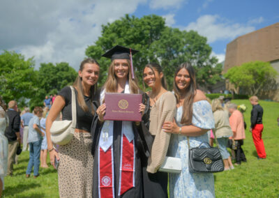 a student holds their diploma cover while standing with friends