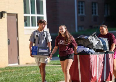 three students with a cart full of items outside a residence hall