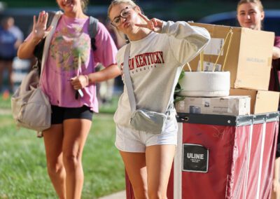 students wave while moving a cart filled with move-in items