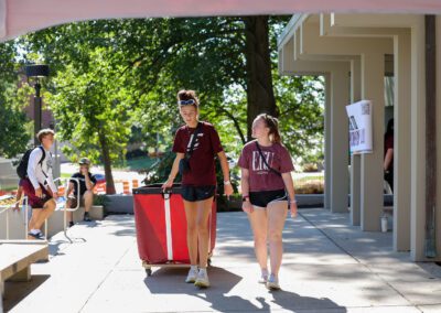 two students with a cart outside a residence hall