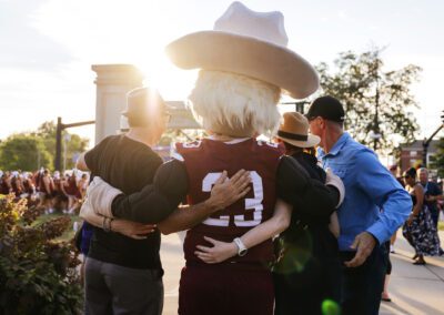 the sun shines over the Colonel mascot and three people during the Big E Welcome Walk