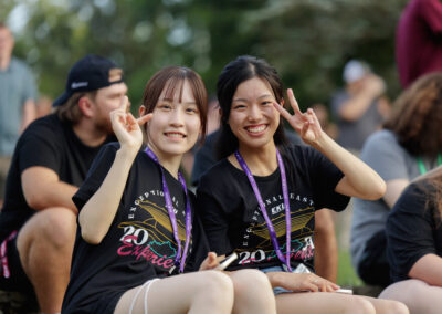 Two dark haired students smile and give peace signs awaiting Flo Rida outdoor concert