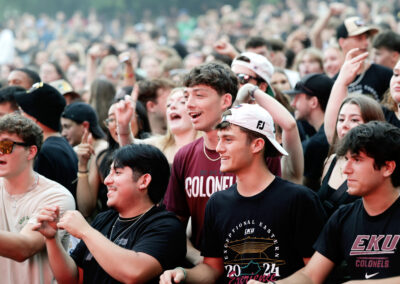 A group of male students wearing EKU shirts and hats smile while watching the stage at the Flo Rida outdoor conference