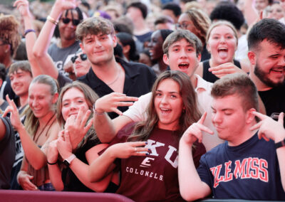 Excited female student models EKU shirt with a crowd of happy students surrounding her at the Flo Rida outdoor concert