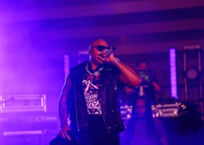 Flo Rida, in sunglasses, raps into sparkling microphone with purple backlighting at outdoor concert