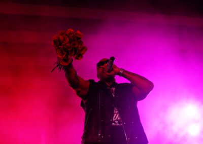 In the dark, with pink and red lights behind him, Flo Ride raps to the student crowd while raising a handful of roses at the outdoor concert