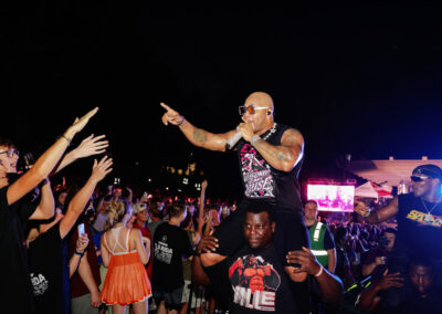 Flo Rida rides on man's shoulders while rapping and pointing to the crowd of EKU students in the dark at the outdoor concert