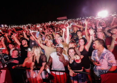 Large crowd of EKU students at night, celebrating with glow sticks and phone lights in the air at the Flo Rida outdoor night time concert