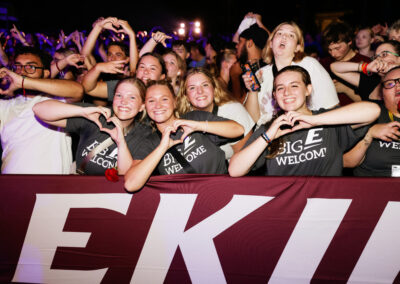 A group of smiling, happy female EKU students make hearts with their hands on the front row of the night time outdoor Flo Rida concert