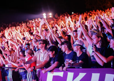 A very large crowd of excited EKU students at night raise their hands and cheer at the outdoor night time Flo Rida concert