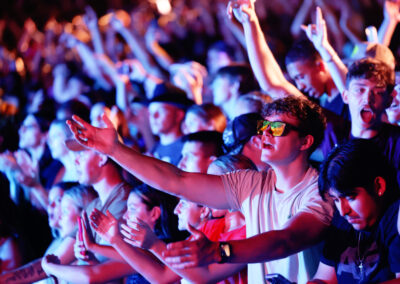 A crowd of EKU students, one in sunglasses, at night sing along and raise their arms in the lights of Flo Rida outdoor concert