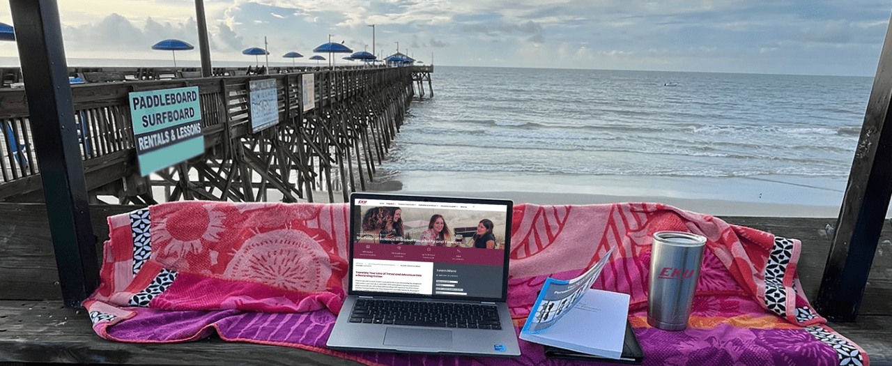 a laptop with an EKU website overlooking a pier at the ocean