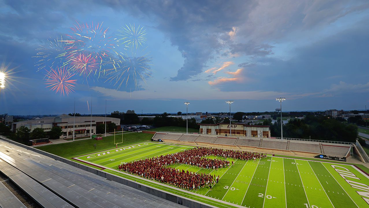 fireworks go off above students forming the Big E on the football field