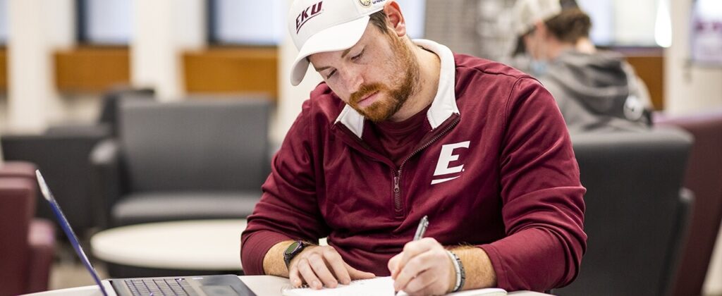 Male EKU student works online to complete coursework in the library.