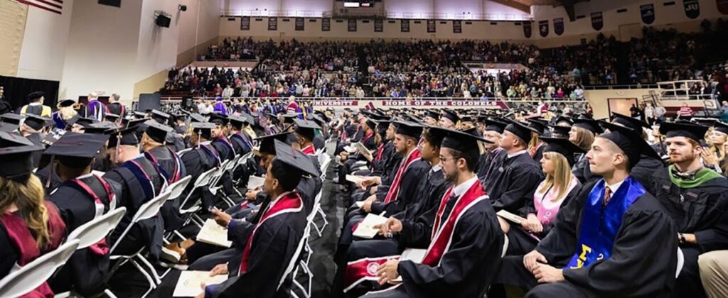 Side view of EKU graduates in caps and gowns sitting in Alumni coliseum for commencement services.