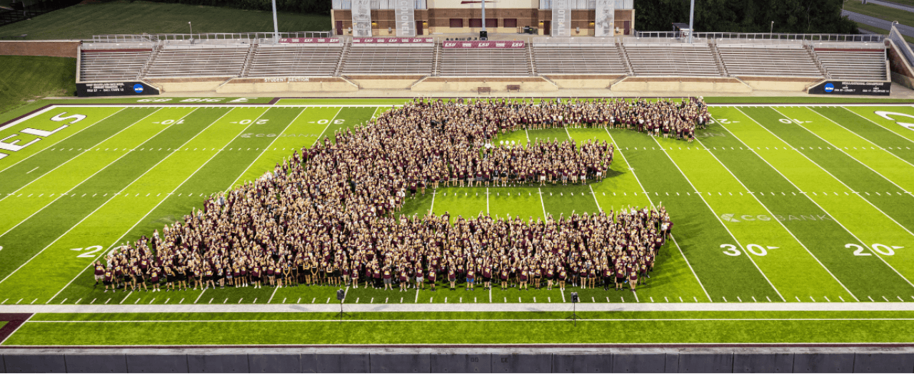 The 2023 freshman class stands on the football field to form the EKU Power E logo at night.