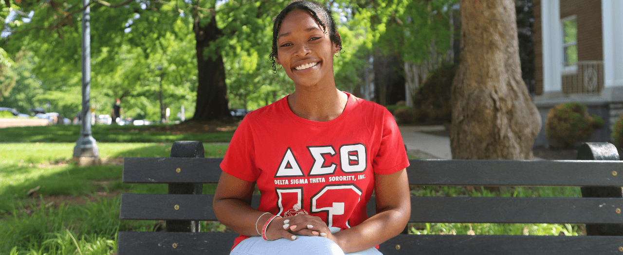 EKU Student Ainye Rogers sits on a bench on campus, smiling.