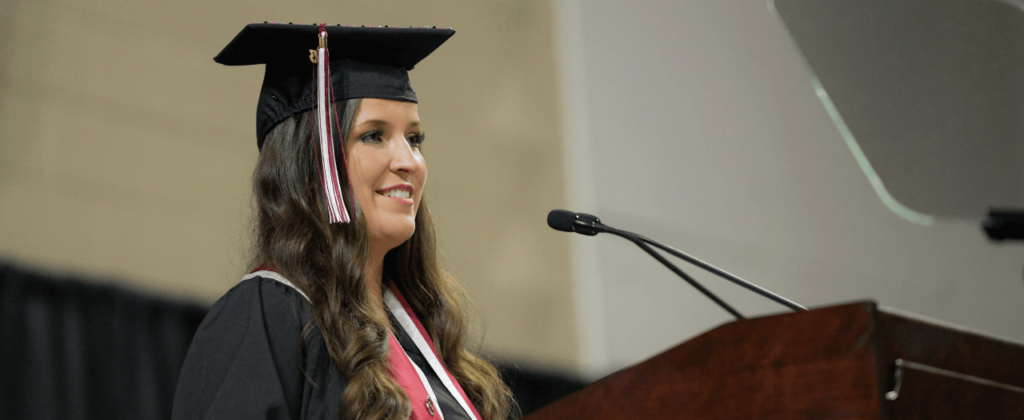 EKU graduate Haley Snell, in cap and gown, stands at the podium and smiles at the crowd at graduation.