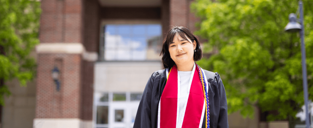 Smiling EKU graduate Chia Hui Ouyang (Joanna) stands in her regalia in front of EKU's Business and Technology Center.