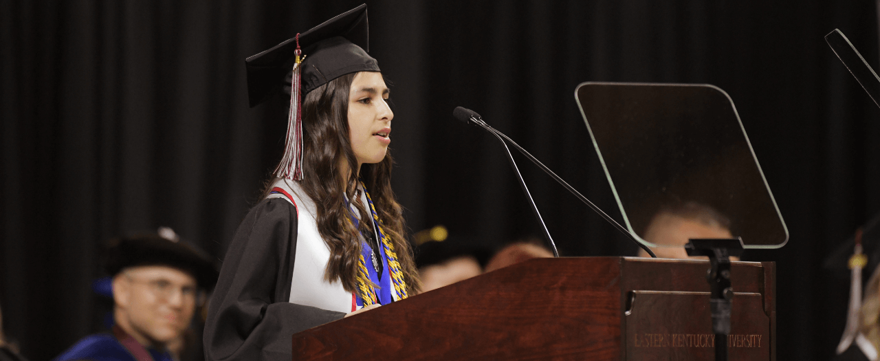 EKU commencement speaker, in graduation regalia, stands at the podium and delivers her message during the ceremony.