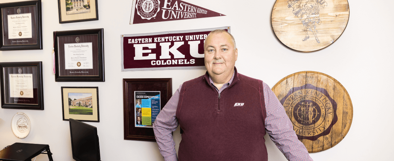 EKU Global Supply Chain Management professor, Kirby Easterling, stands in front of his EKU memorabilia wall in his office.