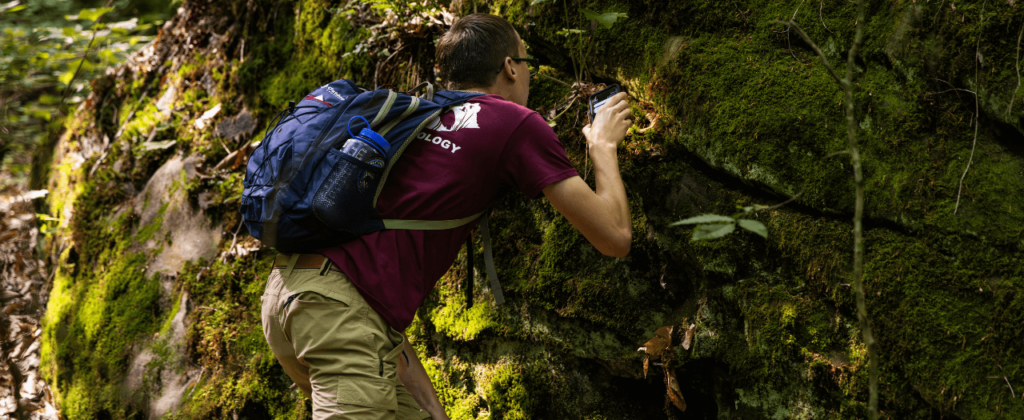 EKU student examines moss on a rock in the forest.