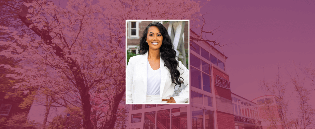 Dr. Annabelle Manol-Morgan, dressed in a white suit, stands with a hand on her hip in front of a campus building.