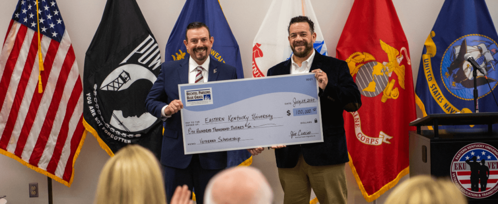 EKU President David McFaddin accepts a scholarship contribution from Bechtel Parsons in front of a display of military flags.