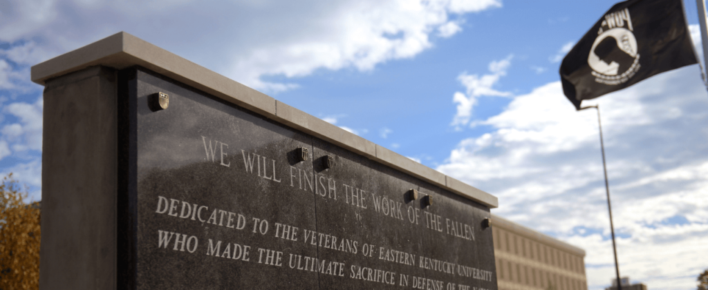 An upward view of EKU's Veteran Memorial with the blue sky and POW MIA flag in the background.