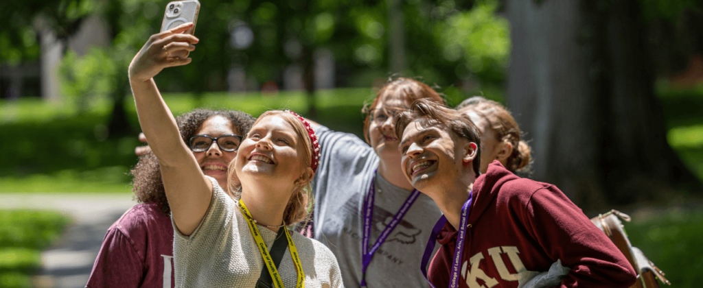 Five incoming EKU students gather around one with a phone to take a selfie outdoors on campus.