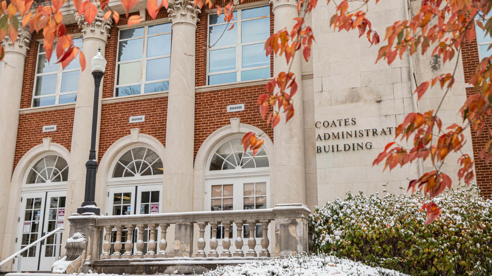 the Coates Administration Building entrance with autumn leaves and a dusting of snow