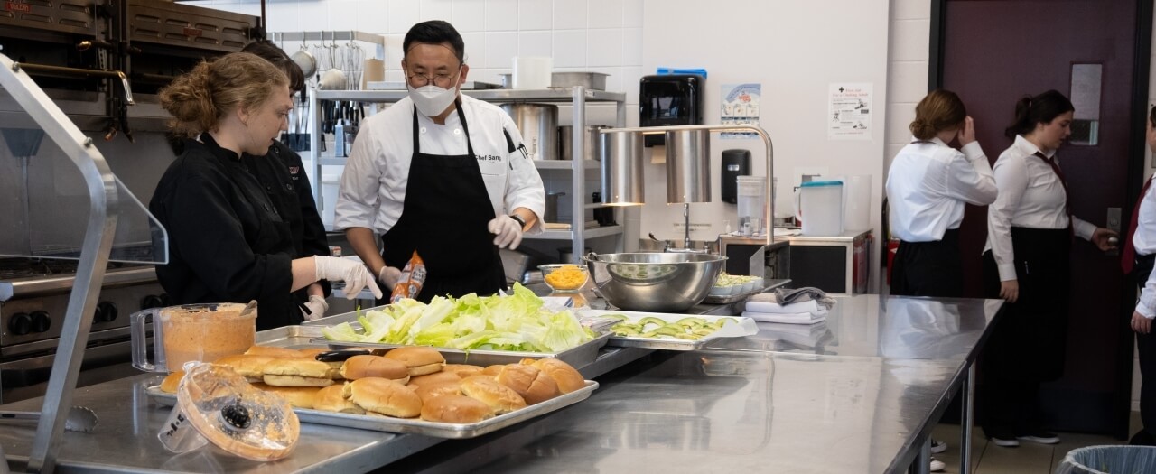 Two students work in the commercial grade kitchen with Chef Sang to prepare lunch at Cafe Burrier.