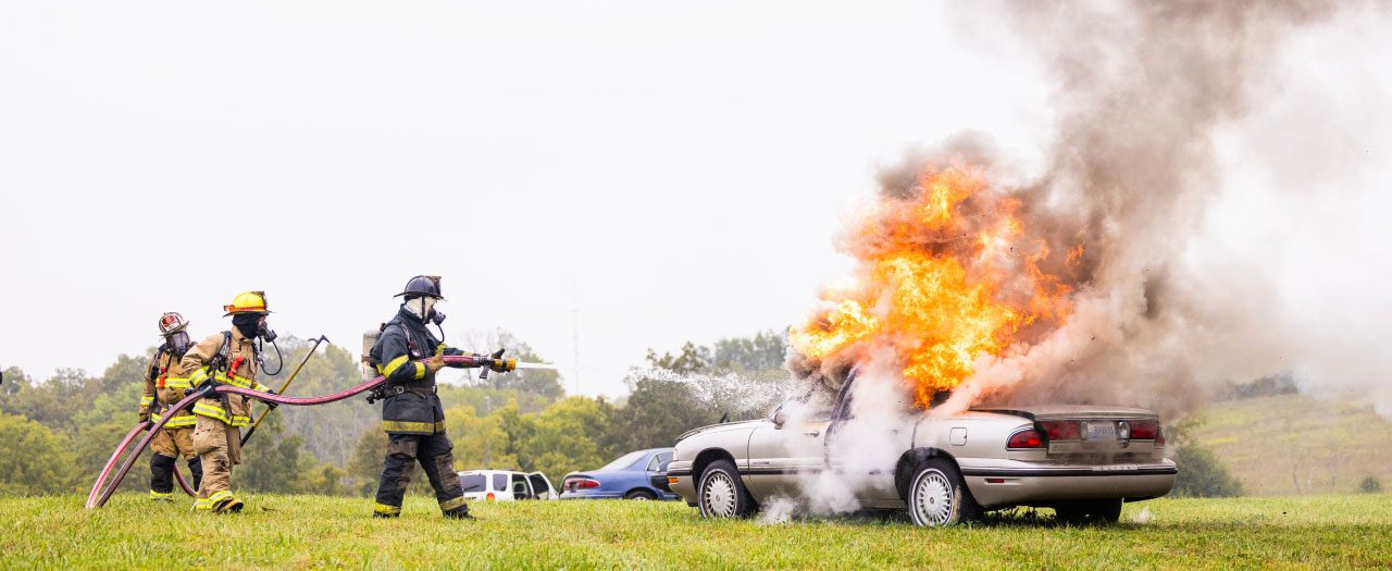 firefighters spray water on a car fire