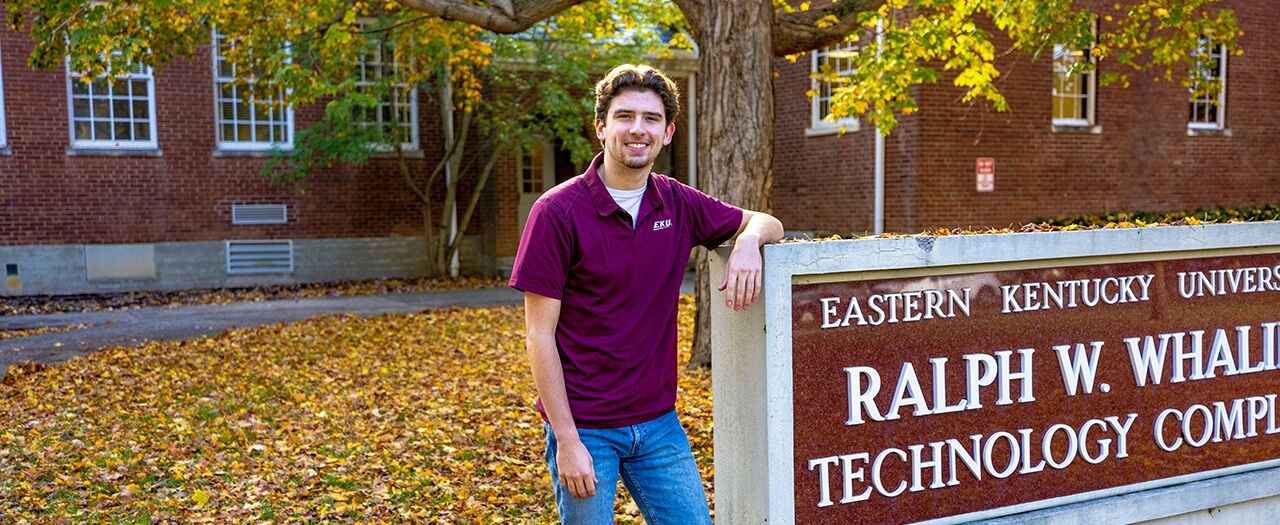 EKU manufacturing engineering student, Davis Huntley rests against the Ralph W. Whalin Technology Complex sign on EKU's campus in fall.