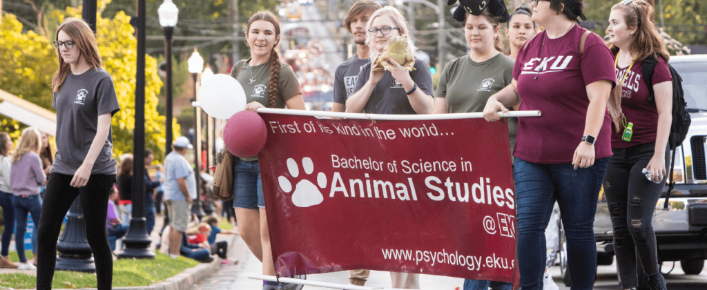 A group of EKU animal studies students hold a banner promoting EKU's program in the Homecoming parade.