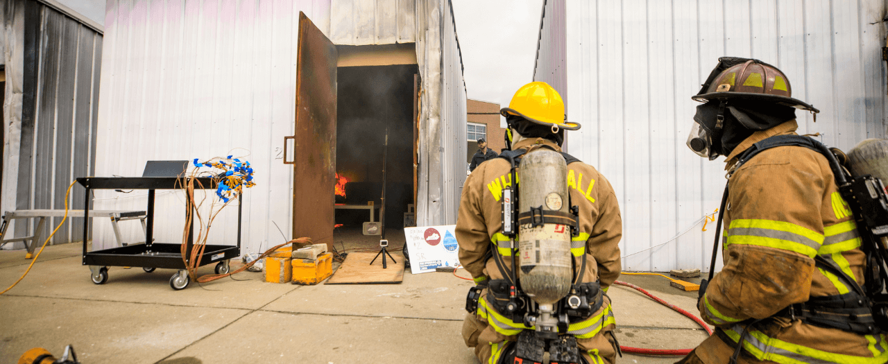 Two EKU firefighter students wear protective gear and monitor a burn at EKU's fire investigation lab.